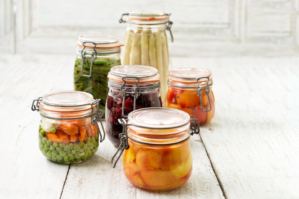 Bocaux en verre remplis de légumes et fruits conservés sur une table en bois blanc