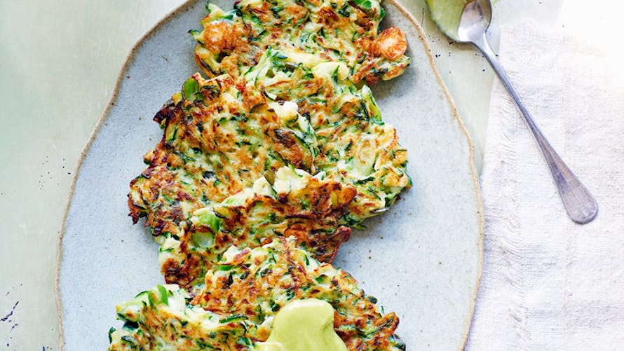 Galettes de courgettes sur assiette avec tranche de citron et cuillère.