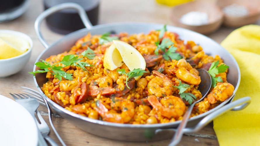Paella aux crevettes dans une poêle sur une table en bois.