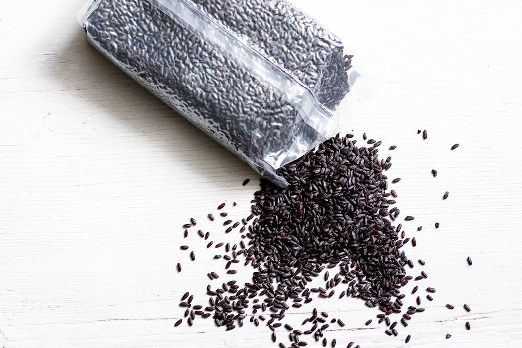 Sachet ouvert de riz noir venere renversé sur fond blanc.