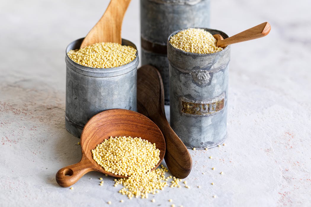 Grains de millet dans des récipients en métal et une cuillère en bois.