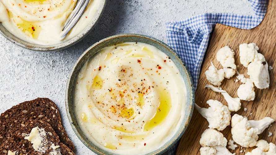 Purée de chou-fleur dans des bols, pain complet et chou-fleur cru sur planche en bois.
