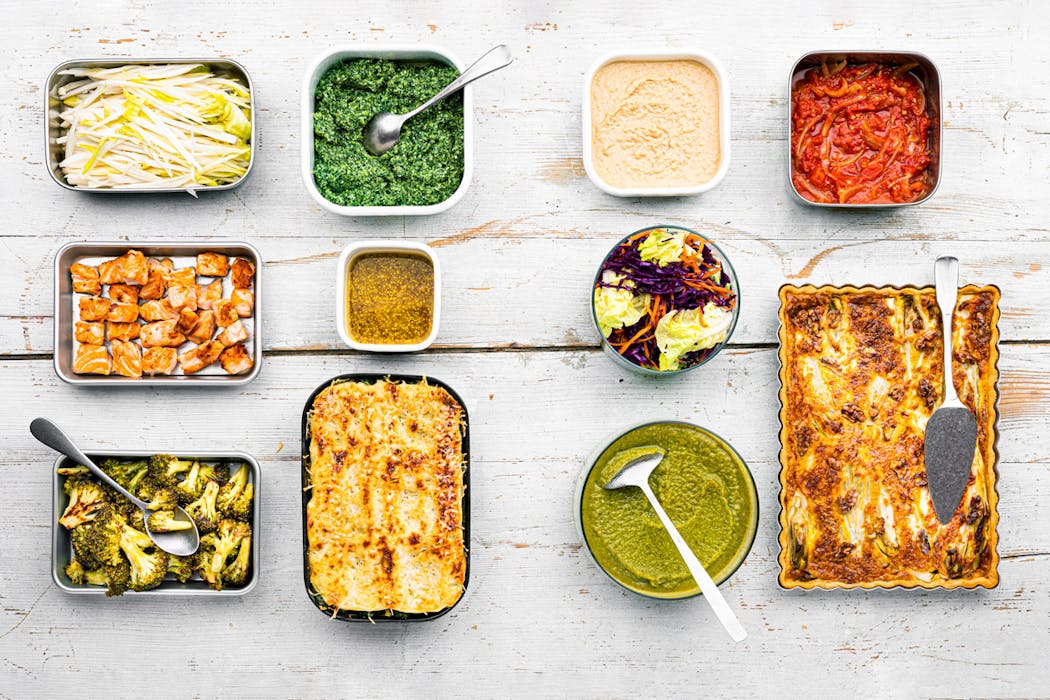 Plats variés dans des récipients sur une table en bois, incluant lasagnes et sauces colorées