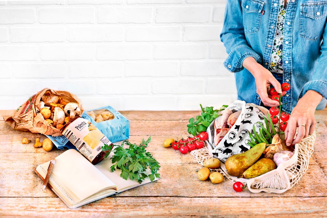 Retour de courses : une personne range des légumes et fruits dans un sac en filet sur une table en bois